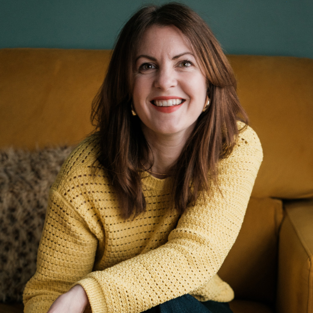 Kelly Molson, Agency Advisor smiles at the camera wearing a yellow sweater while sitting on a brown sofa.